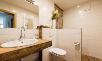 A modern bathroom with a wooden vanity and bright tiles. There is a shower and stylish decoration with plants.