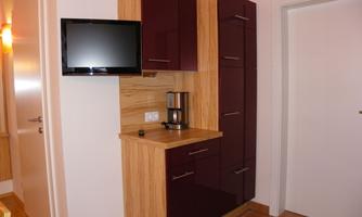 A modern kitchen corner with wood and dark purple cabinets. A television and a coffee pot are also available.