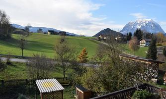 A picturesque landscape with gentle hills, trees, and scattered houses. Snow-capped mountains can be seen in the background.