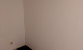 An empty wall with a coat hook shelf above it. Below are two black mats.