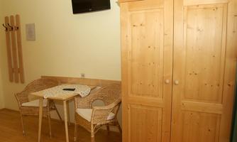 A cozy room with two chairs and a small table. A large wooden cabinet and a TV on the wall complete the decor.