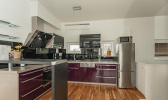A modern kitchen with glossy, dark purple cabinet fronts and high-quality appliances. The floor is made of wood and creates a warm atmosphere.