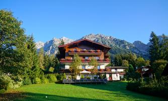 A picturesque Alpine house surrounded by green meadows and mountains. The clear sky creates an idyllic atmosphere.