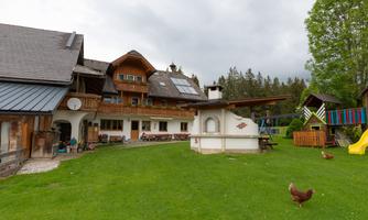 A traditional wooden house with a large garden and lawn area. In the background, there are play equipment for children and some chickens visible.