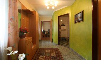 An inviting hallway with green-painted walls and a beautiful carpet. On the left side is a wooden cabinet with plants and other decorative elements.