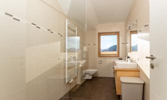 A modern bathroom with bright tiles and a large window front. The amenities include a sink, a toilet, and a towel radiator.