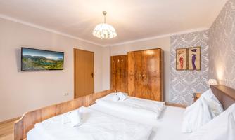 A cozy bedroom with two single beds and a large wardrobe. A television is mounted on the wall, and there is a nice ceiling light.