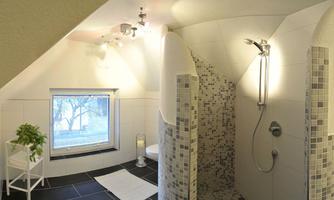 A modern bathroom with an elegant shower and large windows. The walls are light tiled, and the floor is made of dark tiles.