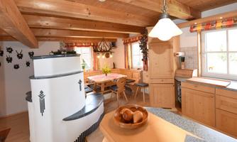 A bright kitchen with a wooden ceiling and furniture. In the center is a modern fireplace stove and a dining table with chairs.