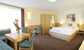 A bright room with wooden furniture and a cozy atmosphere. The room features a double bed, a table, and comfortable chairs.