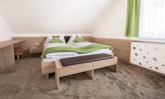 A bright bedroom with a double bed and green bedding. The room has a cozy atmosphere and large windows with green curtains.
