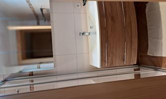 A modern bathroom with a shower and an elegant wooden sink. The walls are tiled in light colors and there is a soft carpet on the floor.