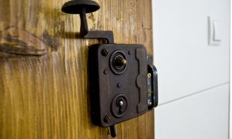An old metal door lock on a wooden surface. The construction features a key mechanism and a robust design.
