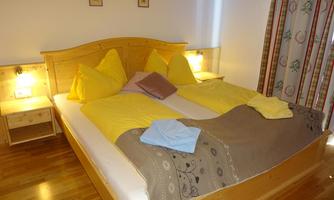 A cozy bedroom with a large bed and yellow pillows. Next to the bed is a nightstand with a warm light.