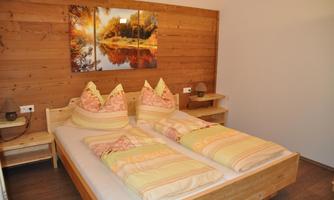 A cozy bedroom with a wooden interior and a double bed. A picture of an idyllic landscape hangs on the wall.
