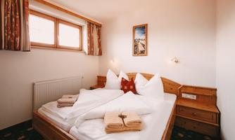 A cozy bedroom with two single beds and fresh towels. The room has a friendly atmosphere and large windows for plenty of daylight.