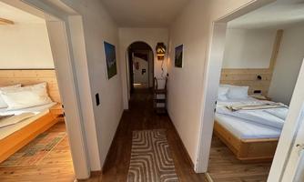 A bright hallway with wooden flooring and a carpet. On both sides are two bedrooms with modern furniture.