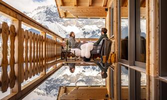 A cozy terrace with a view of the mountains. Two people are relaxing on the porch in a rustic setting.