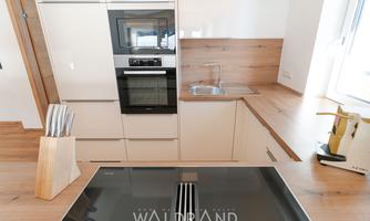 A modern kitchen with bright cabinets and a wooden countertop. In the foreground is a kitchen island with a cooktop.