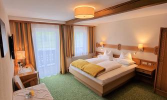 A cozy hotel room with two beds and a yellow pillow. The room has large windows and a green carpet.