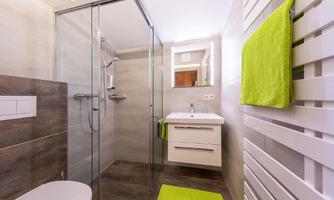 A modern bathroom with a glass shower and a bright sink. Green accessories, such as towels and a bath mat, add color to the space.
