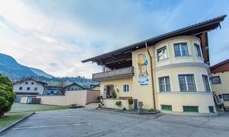 A charming building in the Alps with a large balcony. The surroundings showcase a picturesque landscape and gentle hills.