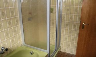A bathroom with a shower cubicle and a bathtub. The walls are decorated with light tiles.