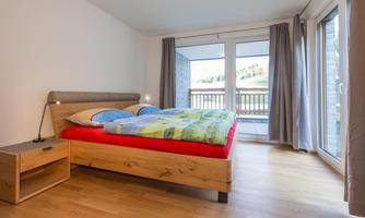 A bright bedroom with a large bed and a beautiful view of the balcony. The walls are kept neutral and the floor is made of wood.