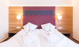 A modern bedroom with two single beds and warm wooden paneling. The decorative cushions and soft light sources create an inviting atmosphere.