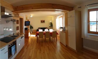 A bright and modern kitchen with an open living area. There is a dining table with chairs and large windows that let in plenty of daylight.