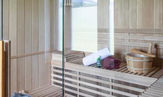 A modern sauna with wooden paneling and large glass windows. Towels and sauna equipment are lying on the bench.