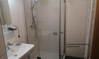 A modern bathroom with a glass shower and a sink. The walls are brightly tiled, and the space feels clean and inviting.