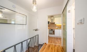 A bright hallway with modern design and wooden flooring. An open kitchen is visible in the background.