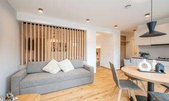 A modern living kitchen with a gray sofa and wooden flooring. The room is bright and friendly, with a dining table and chairs.