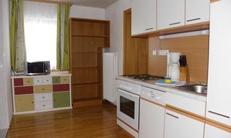A modern kitchen with wooden flooring and white cabinets. There is also a microwave and a refrigerator in the corner.