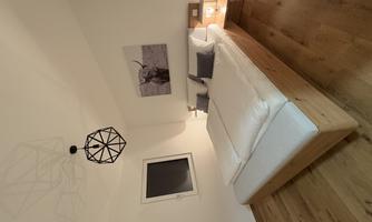 A modern bedroom with a large bed and wooden floor. A picture of an ox hangs on the wall and a geometric lamp provides lighting.