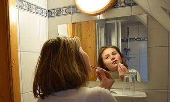 A woman stands in front of a mirror applying lipstick. The room is bright and friendly designed.