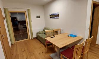 A cozy living space with a table and chairs. In the background, there is a couch and a television.