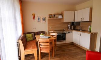 A cozy kitchenette with a dining table and chairs. The walls are light, and there are large windows that let in plenty of light.