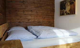 A cozy bedroom with a wooden bed frame and two pillows. A picture of a cow hangs on the wall.