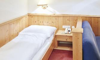 A simple hotel room with a single bed and a blue couch. There is a bedside table with a phone and wood paneling on the walls.