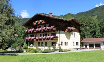 A charming house with flower boxes and a large garden. In the background, there are green hills and a blue sky.
