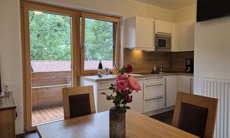 A modern kitchen with wood decor and large windows. On the table, there is a vase with pink roses.