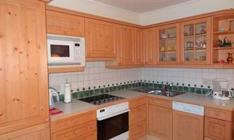 A modern kitchen made of light wood with white appliances. The countertop is well organized and contains cooking utensils.