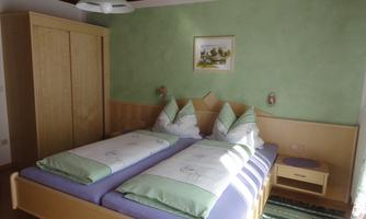 A cozy bedroom with two beds and green walls. There is a wardrobe and a picture on the wall.