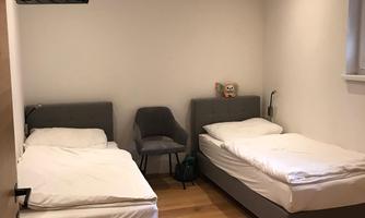 A simple room with two single beds and a chair. A television is hanging on the wall.