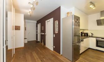 A modern kitchen with a white design and a large refrigerator. The floor is made of light wood, and the walls are partially in neutral tones.