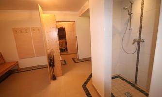 A bathroom with a shower and modern tiles. There is a wooden bench and space for towels.
