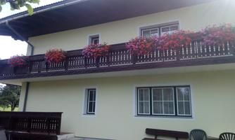 A building with a balcony decorated with colorful flowers. The facade is light yellow and has large windows.