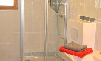 A modern bathroom with a glass shower and a toilet. Towels in red and gray are neatly stored.